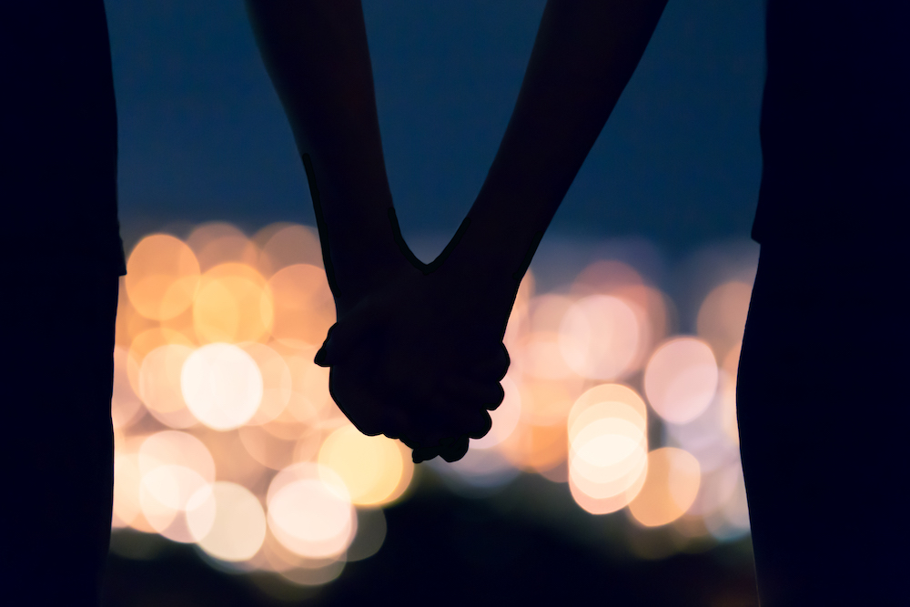 couple holding hands with city lights in background