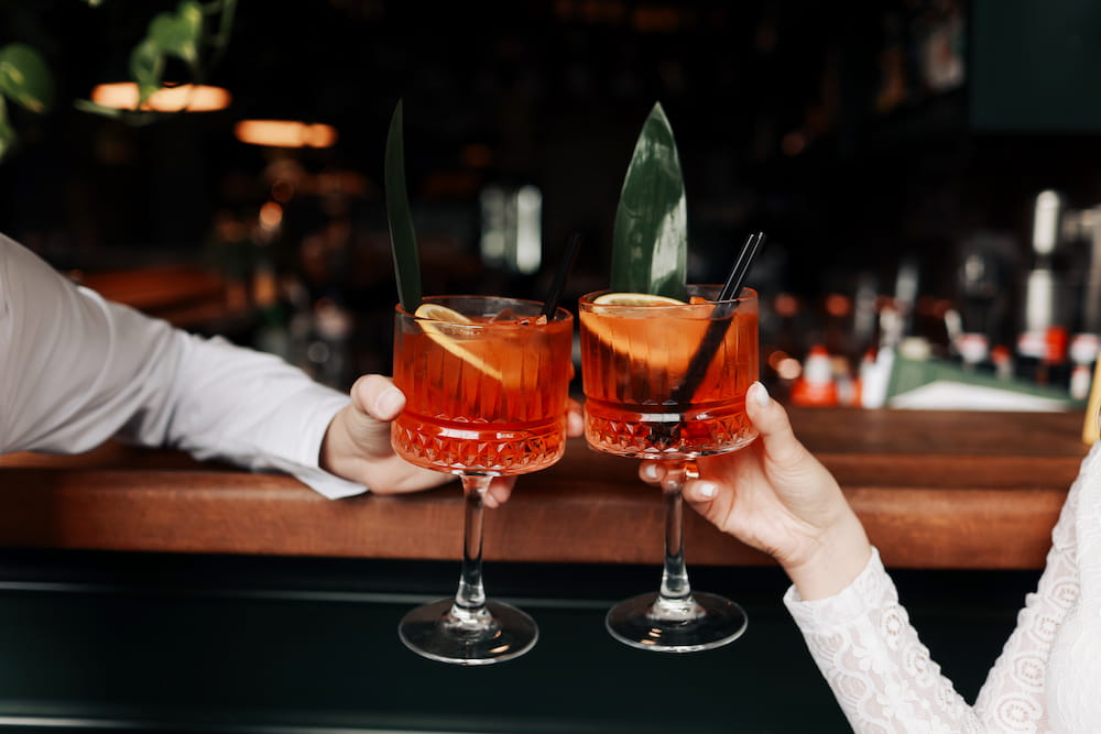 close up of cocktails in a couple's hands as they sit at the bar