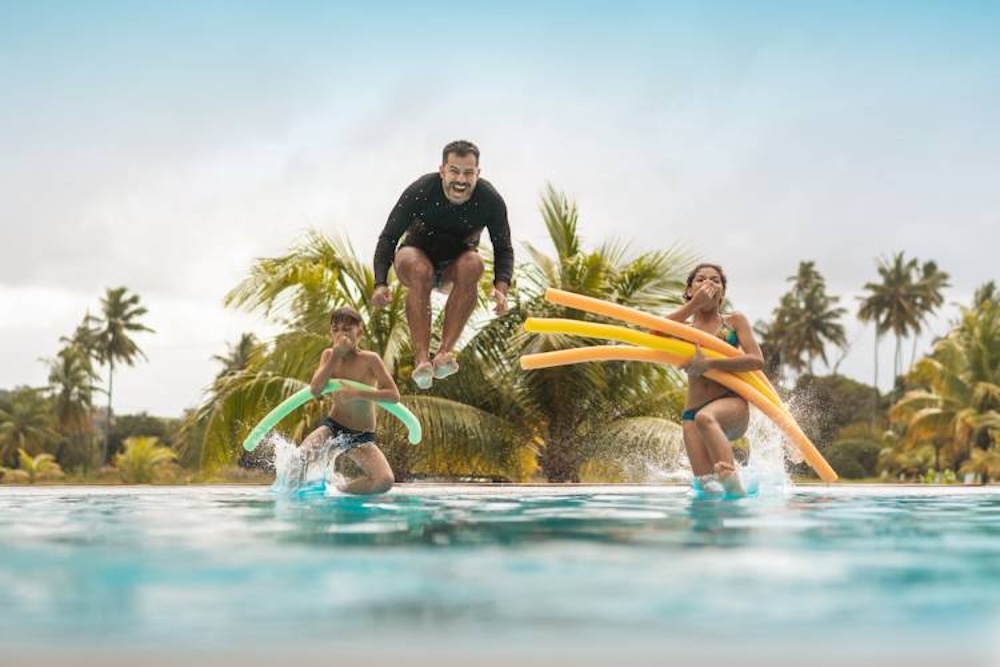 dad doing a cannon ball into a pool with kids jumping behind him