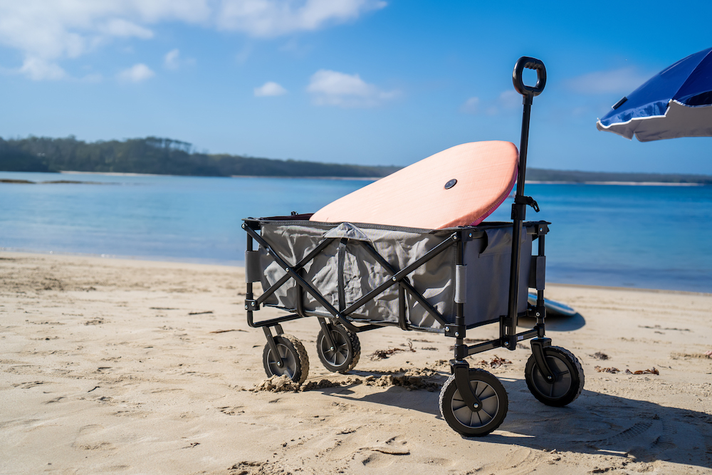 Outdoor beach cart wagon and beach umbrella on a sandy beach near the ocean. Family vacation holidays