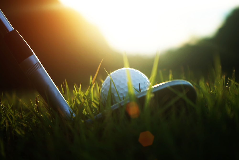 golf club and golf ball close up in grass field with sunset.