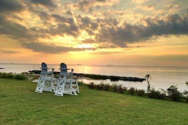 Two empty chairs on green hill facing the water at sunset
