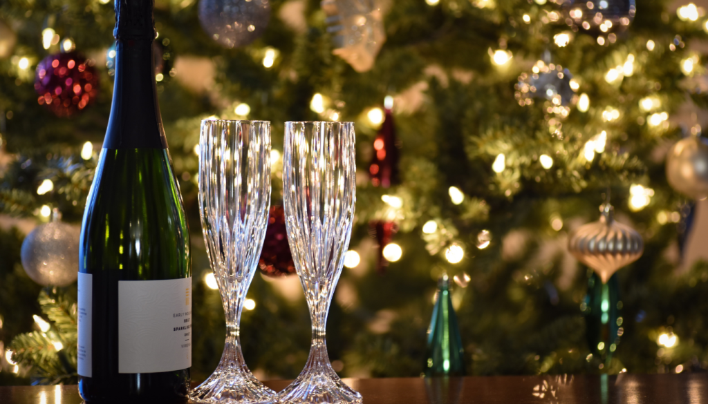 champaign and two glasses in front of lit Christmas tree