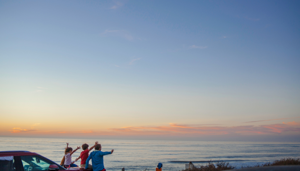family leaning against car overlooking the beach