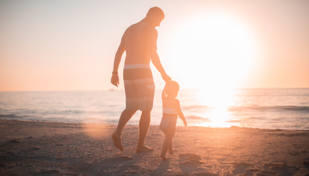 father holding child's hand on beach