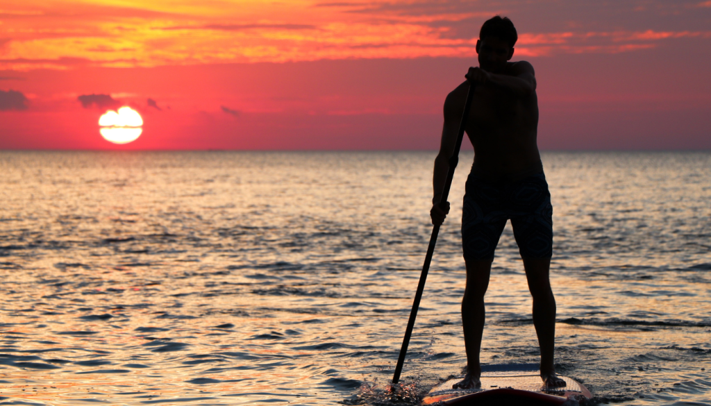 man paddleboarding on the gulf at sunset
