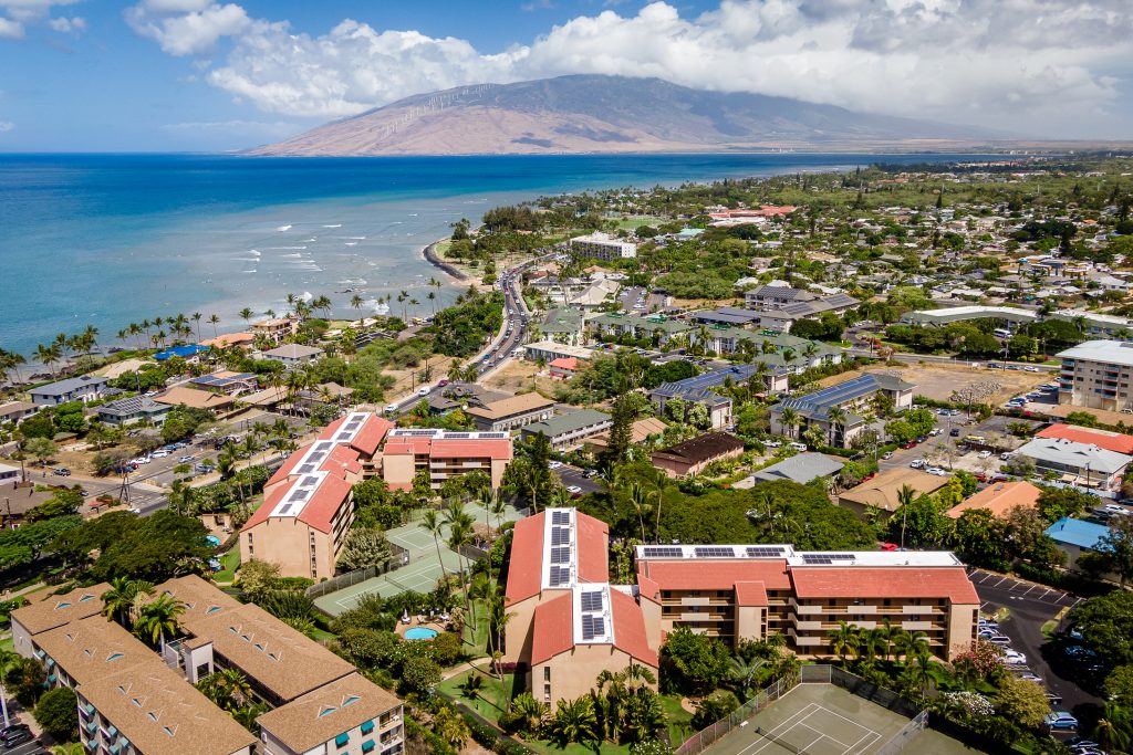 Aerial view of oceanfront condominium buildings on Maui, with the coastline and mountains beyond