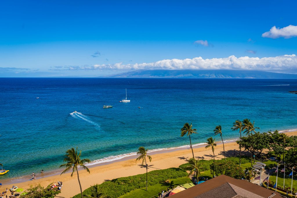 Maui beach and shoreline seen from above, with palms and boats offshore