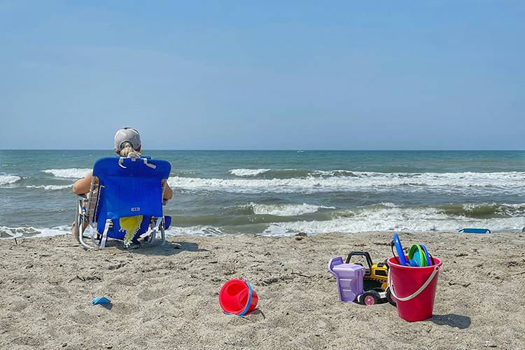 Woman sits on Sandbridge Beach, looking out at the ocean, enjoying her vacation