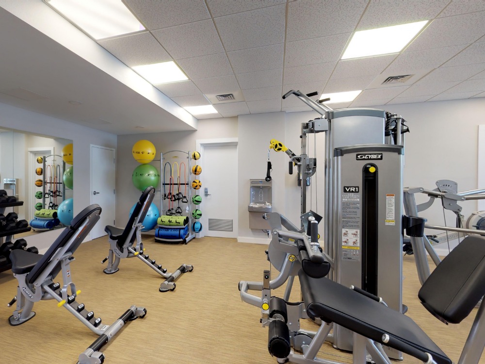 A modern gym interior featuring exercise machines, weights, and colorful fitness balls. Bright lighting and mirrors enhance the space.