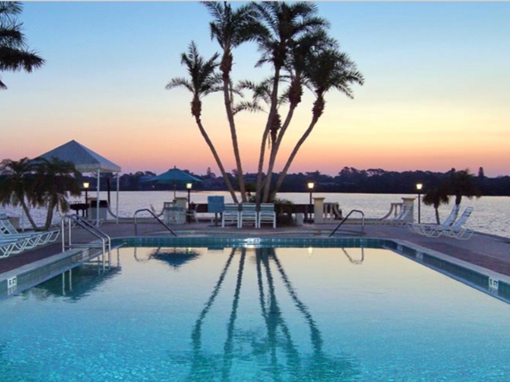 A serene poolside scene at sunset, featuring palm trees and a calm lake in the background.
