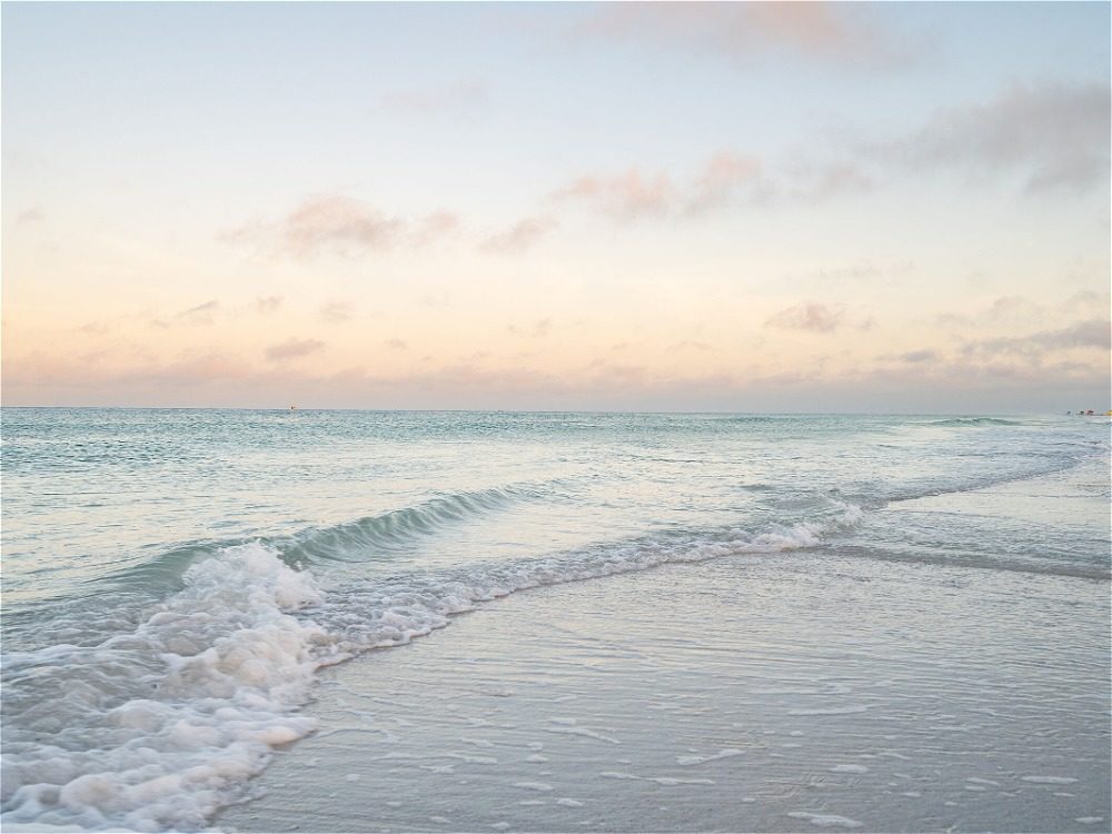 A serene beach scene at sunset, featuring gentle waves lapping at the shore under a pastel sky.