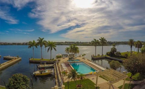 jqg_1556313468 A scenic waterfront view featuring a pool, palm trees, and a boat docked by the shore under a partly cloudy sky.